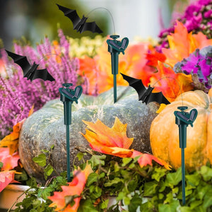 Decorative bats on stakes with pumpkins and autumn leaves in a garden setting