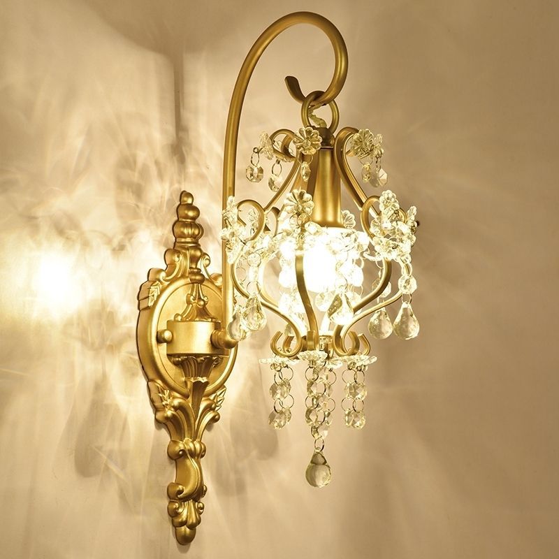 Decorative wall sconce with gold finish and crystal accents on a beige wall.